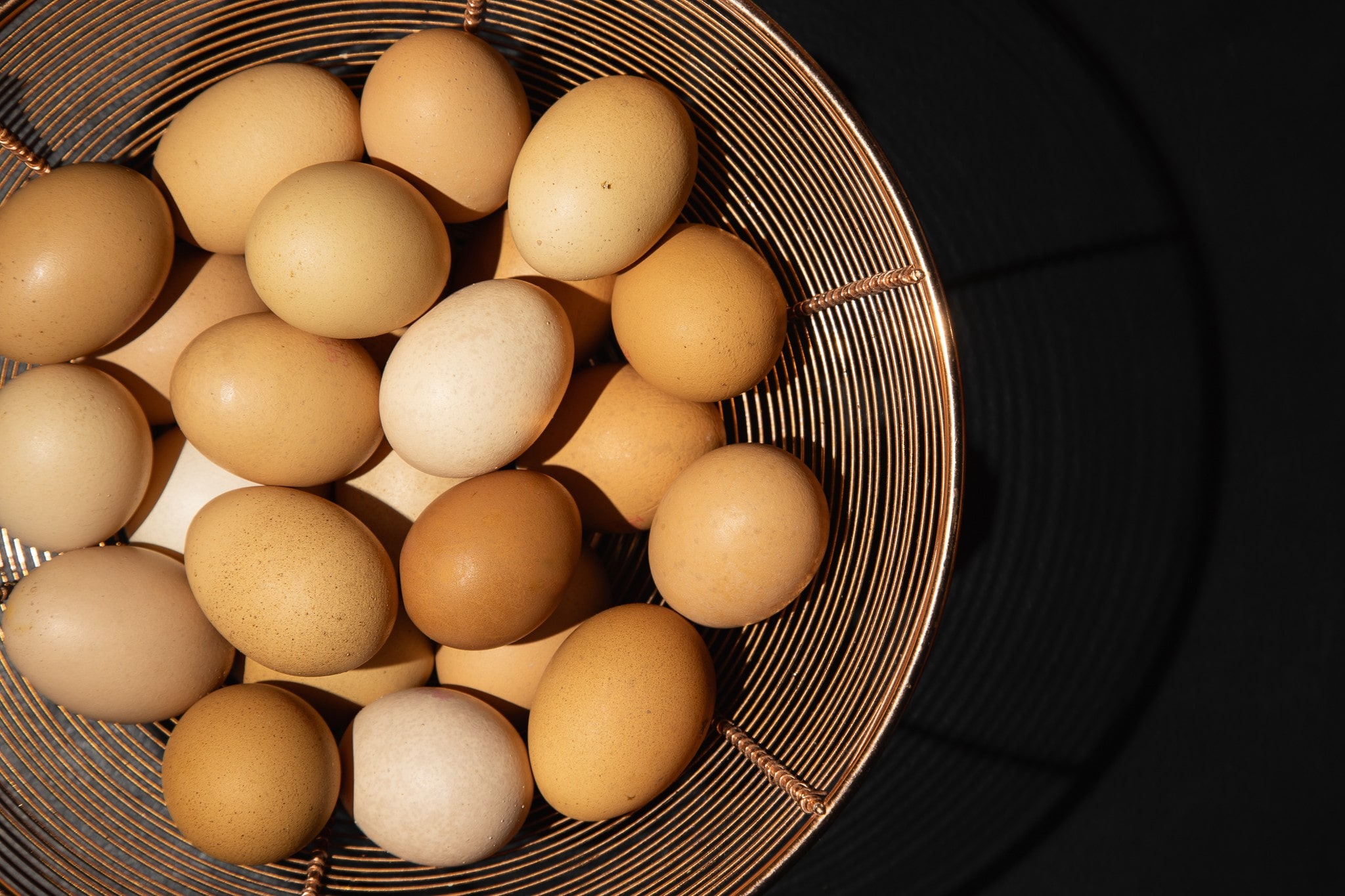 Food Photograph of Fresh eggs gathered in a wire basket against a black background