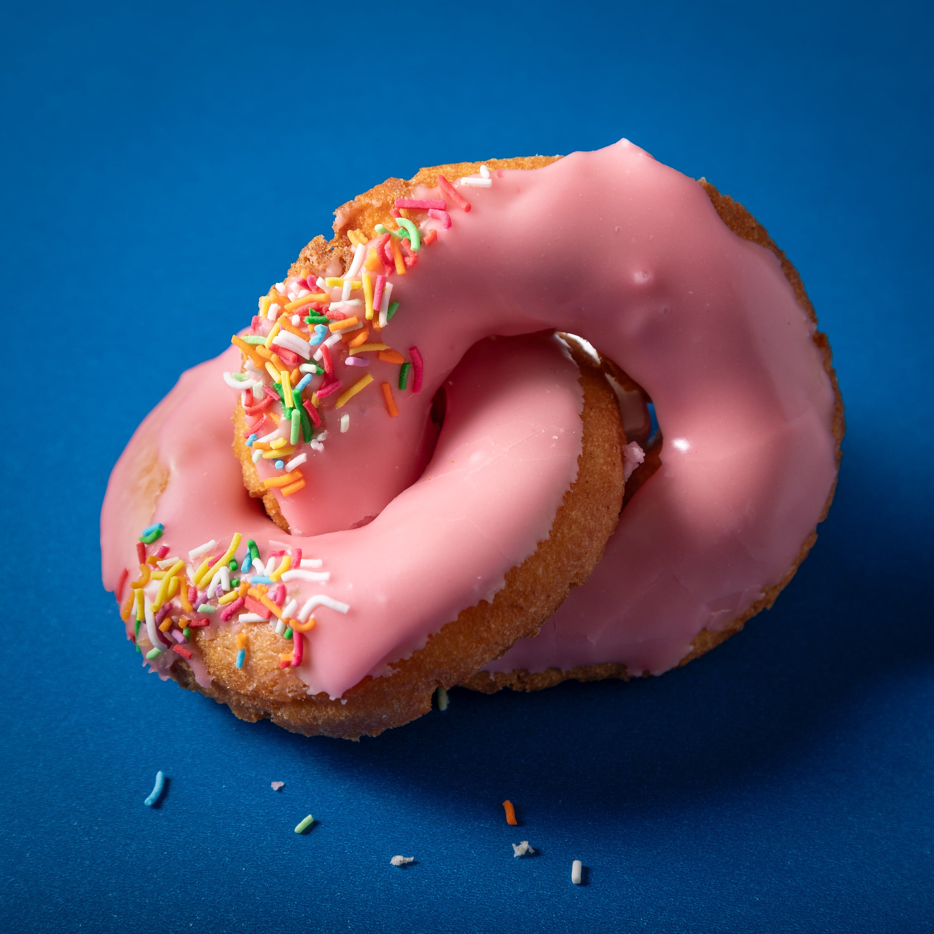 two pink strawberry donuts rings joined on a blue background. Photographed and copyright Steve Wickenton