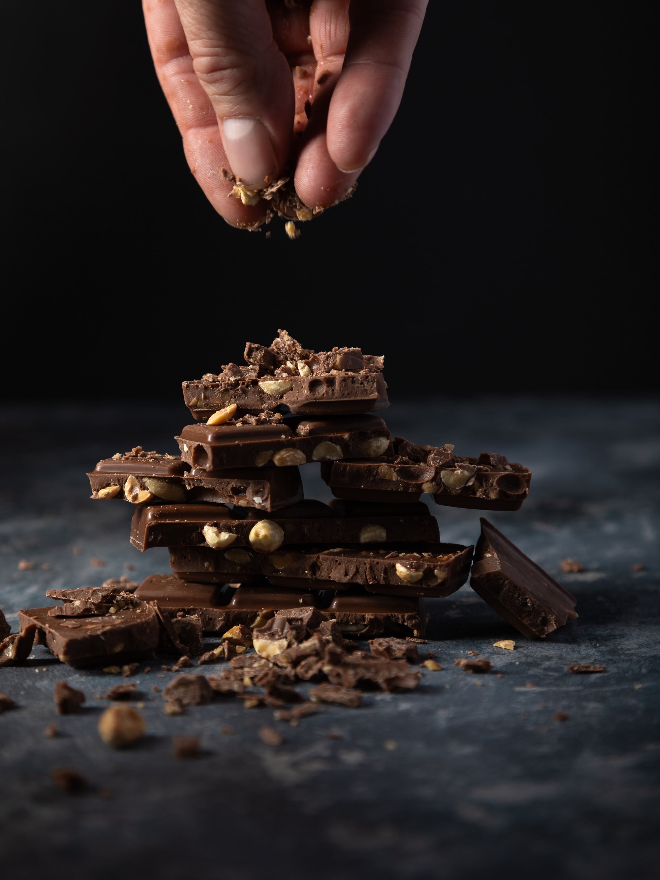 Broken chocolate pieces sprinkled with chocolate crumbs for food photography image. in a dark moody shot.